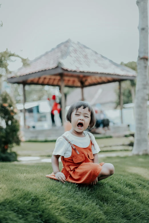 a little girl is laughing while sitting on the grass