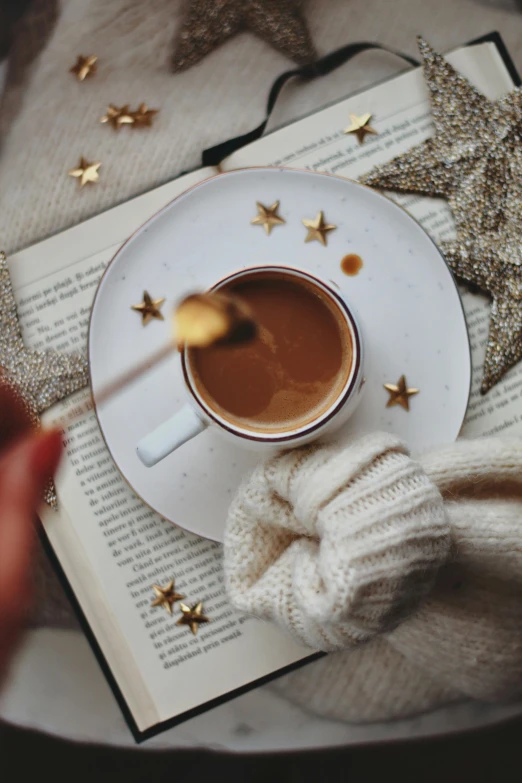 a cup of coffee with gold stars is sitting on an open book