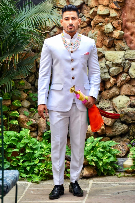 a man in a white suit and a hat stands next to a stone wall