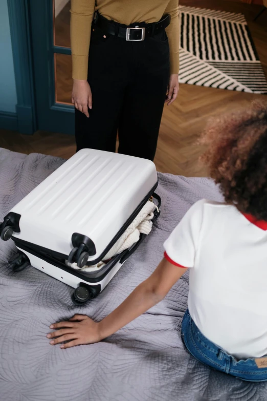 a woman stands next to a luggage bag and a  is sitting on the floor in a bedroom