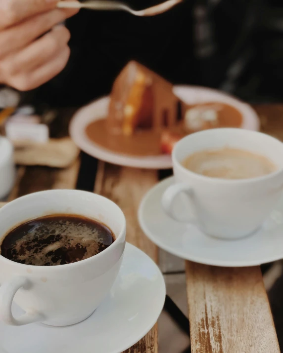 a person holding up a cup of coffee near plates with pastries