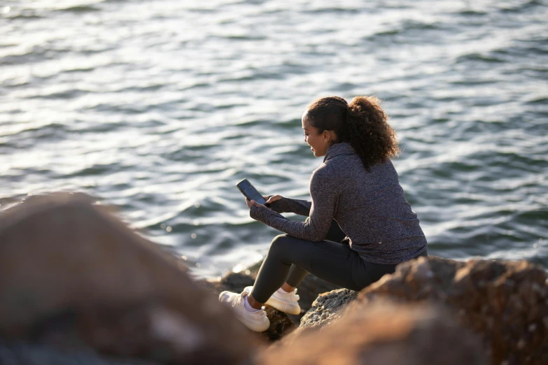 a woman sitting on top of a rock next to the ocean