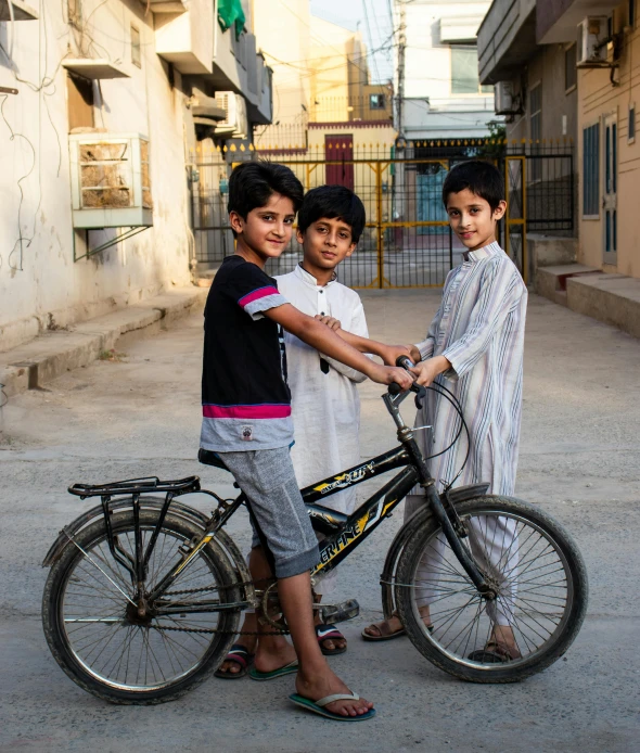 three boys standing next to one another, with a bike