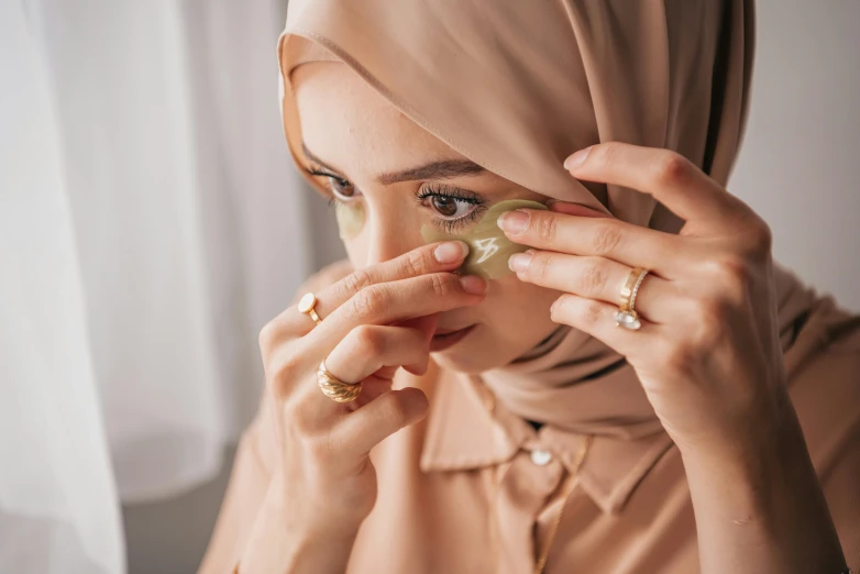 woman in brown hijab putting green jeweled nose ring