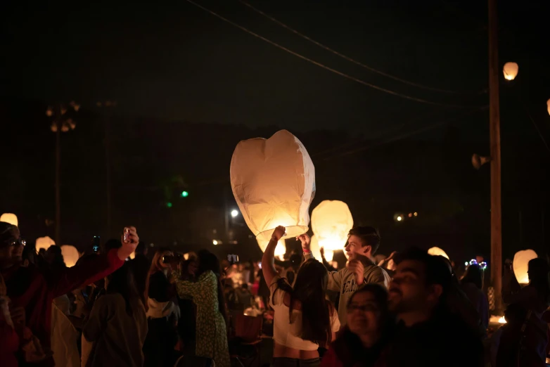 a crowd of people watching a number of small lanterns being flown