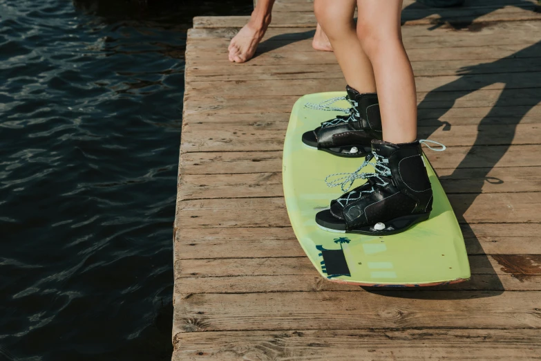 a woman stepping on top of a green board by the water