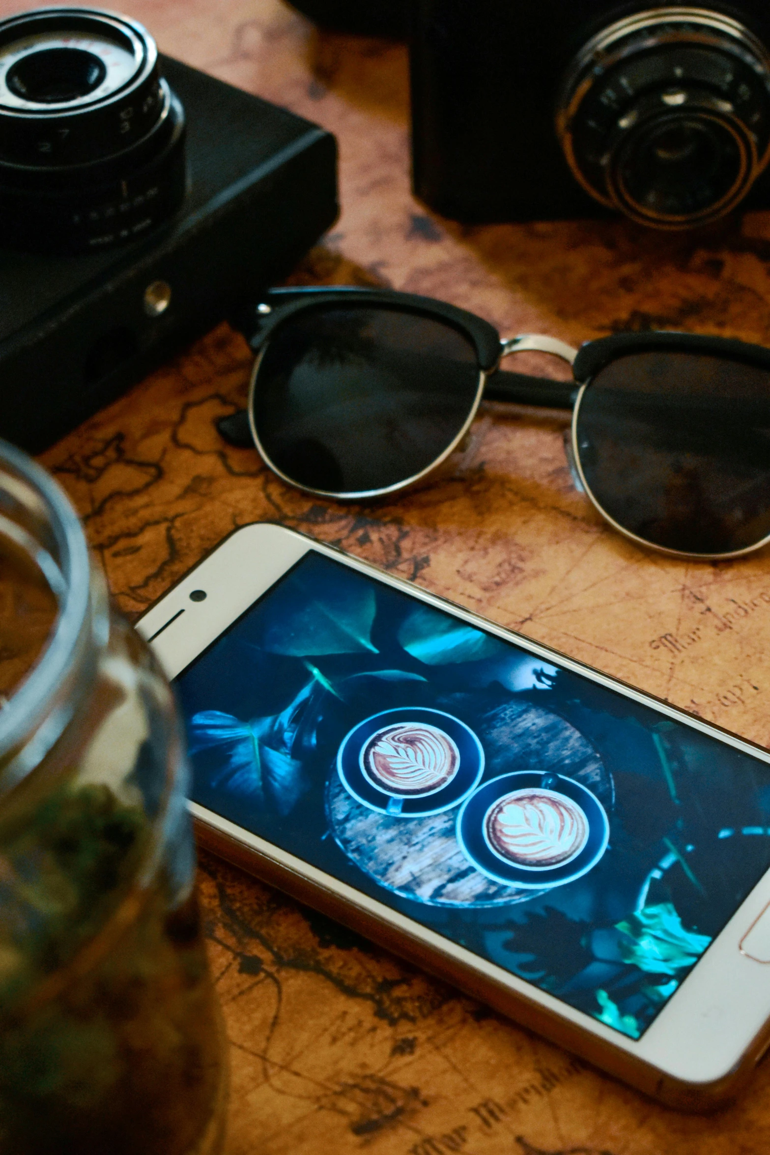 a wooden table topped with a cellphone, sunglasses and camera