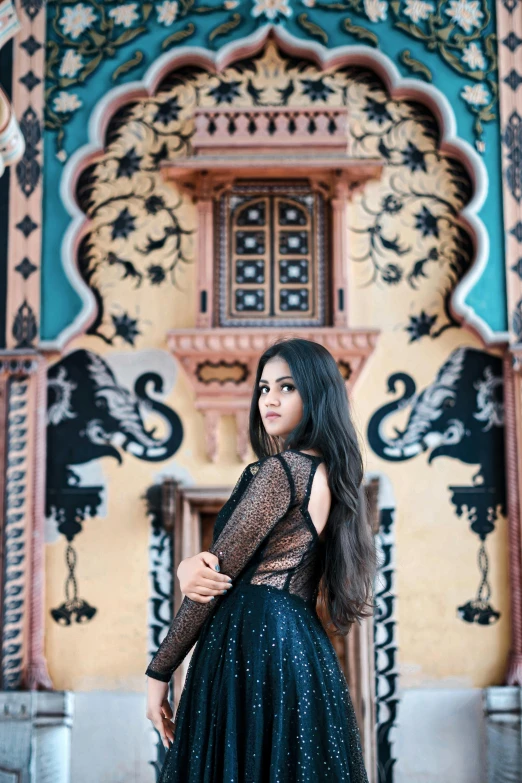 a woman in a long black dress standing by a building