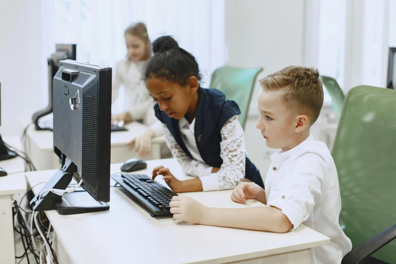 two children looking at a computer screen while one plays on his keyboard