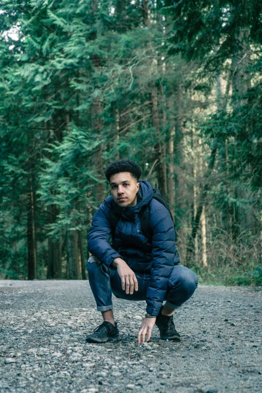 man kneeling on ground next to trees in forest