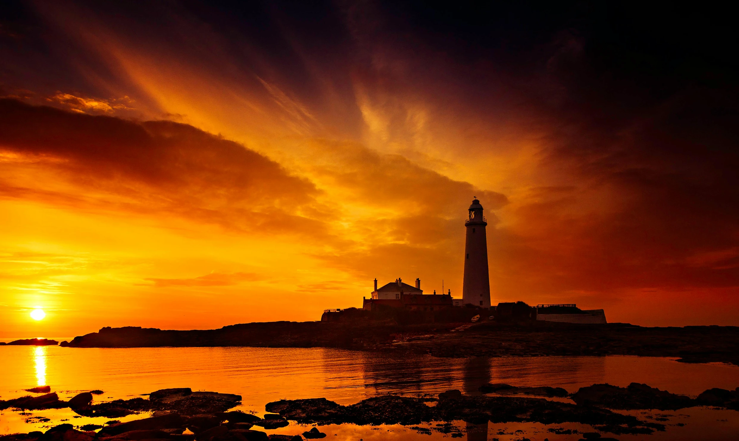 the setting sun behind a lighthouse on the ocean