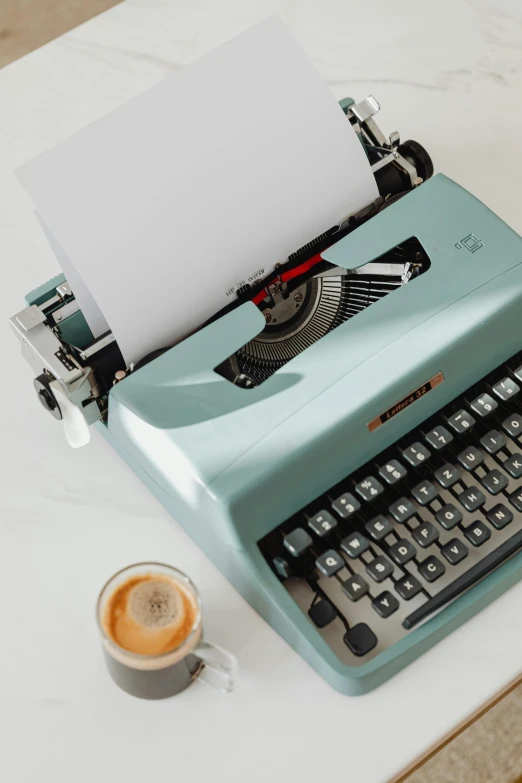 an old typewriter with a paper over it, next to a cup of coffee