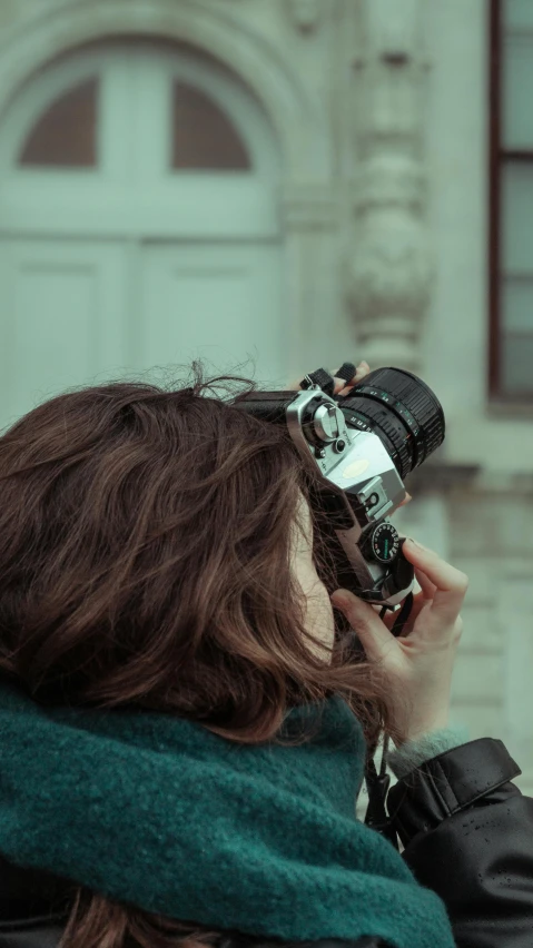 a woman standing on a city street holding a camera to her face