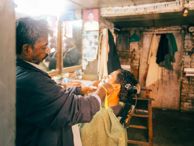 a man shaving a woman's face while she is getting her hair shaved