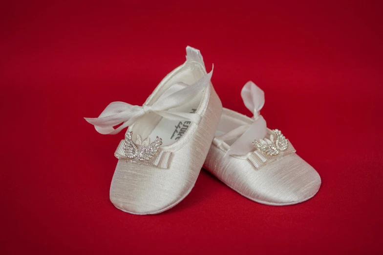 white baby shoes with bows are shown on a red background