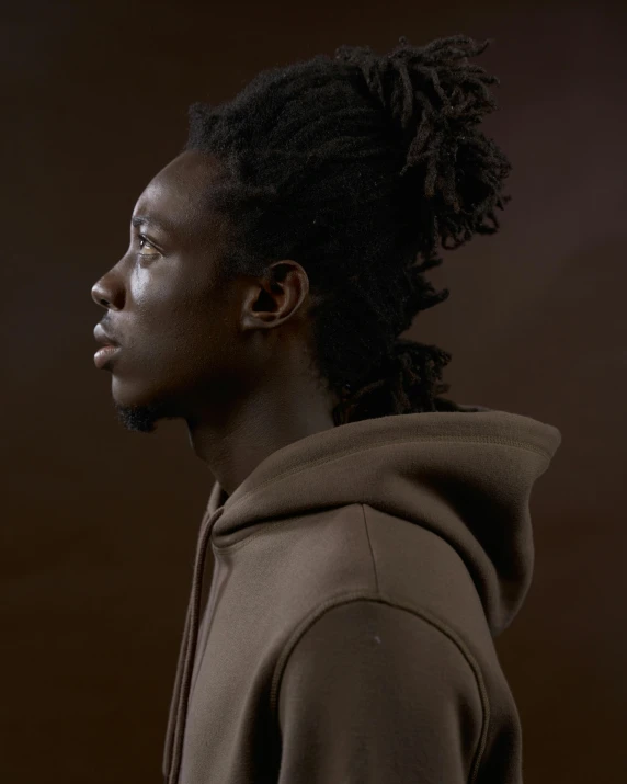 man in hooded jacket with dreadlocks standing against a brown background