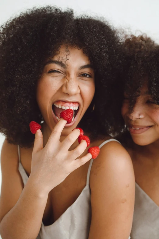 two women in white tops one with red berries on her finger and the other with bright blue eyes