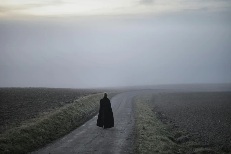 an eerie looking woman in a black robe walking along the road