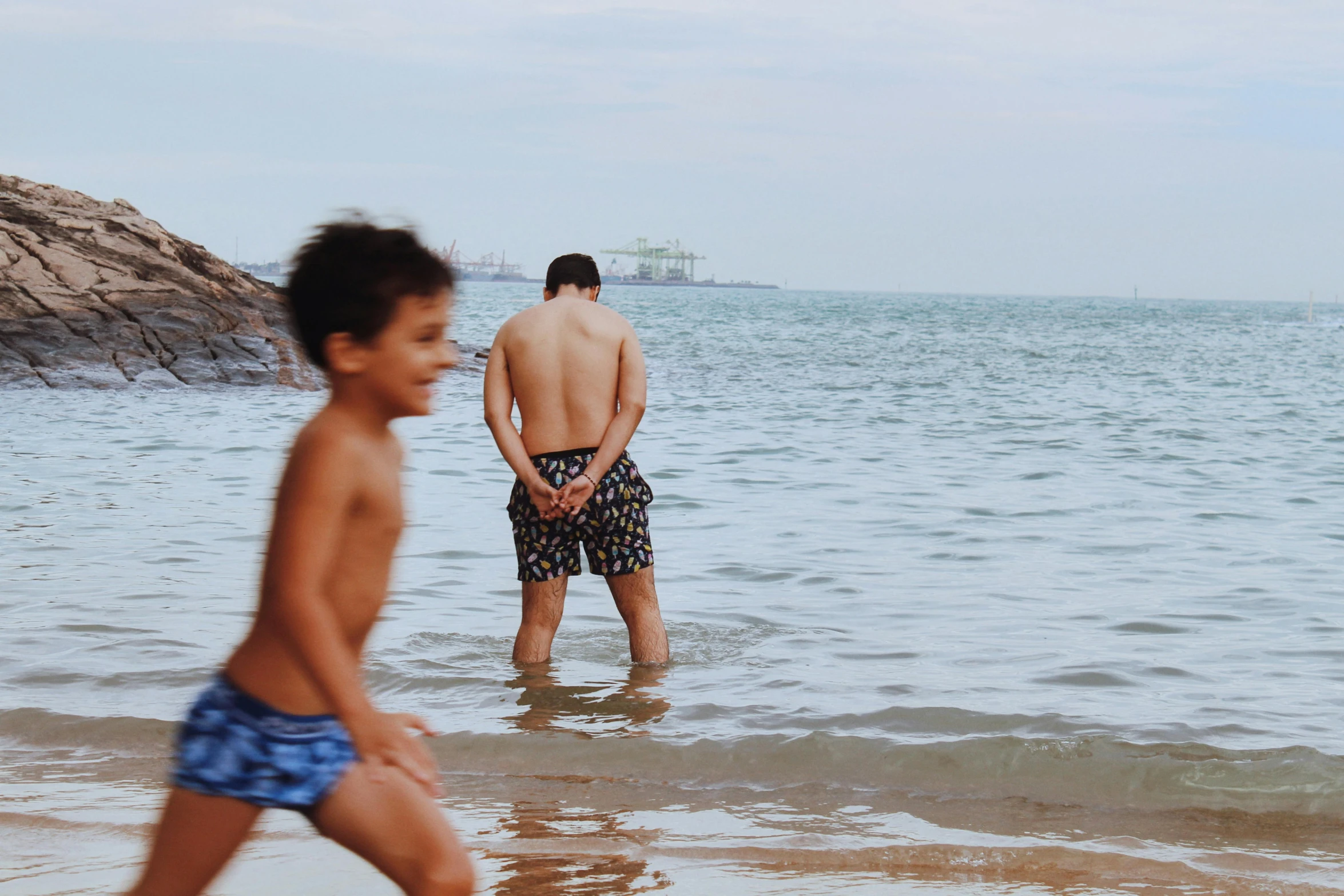 a boy standing next to another child on the beach