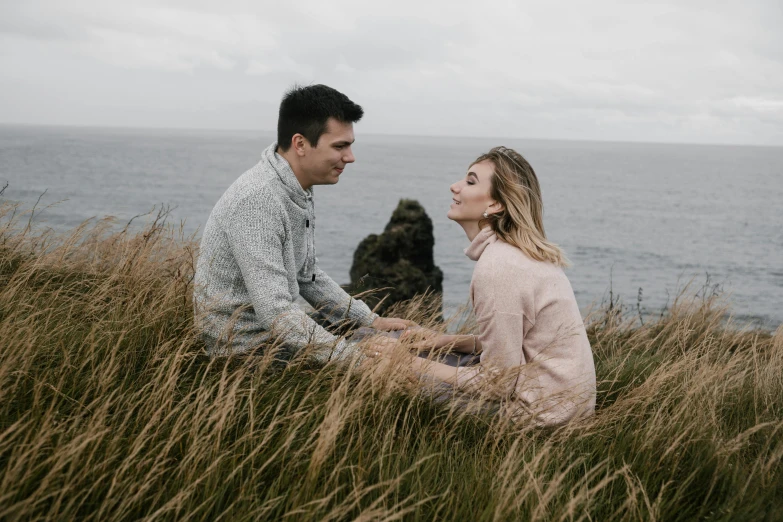 a man and woman are sitting in a grass field, facing each other