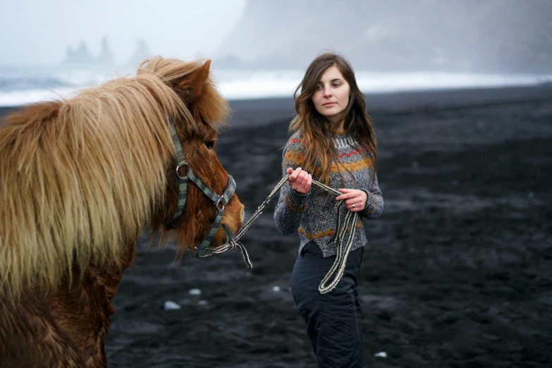 a woman walking with a gy horse next to a large body of water