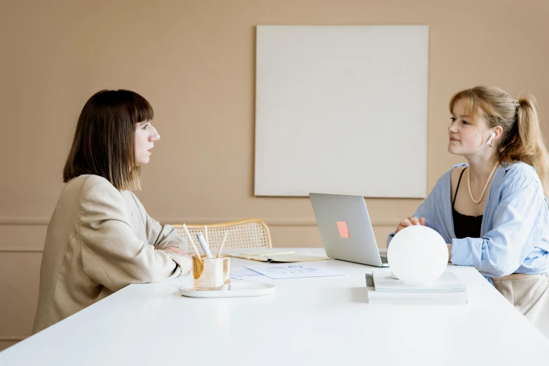 two women sitting at a table looking at soing on a laptop