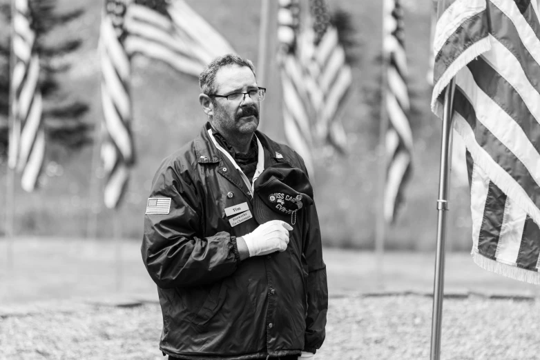 a man with glasses and a beard next to a flag