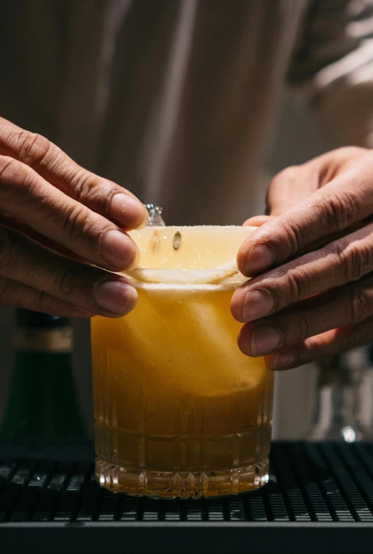 two hands holding a drink in front of some bottles