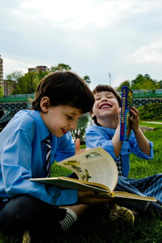 two children laying on the grass reading and laughing