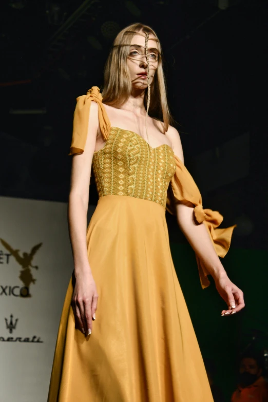 a model wears a yellow dress while walking down the runway