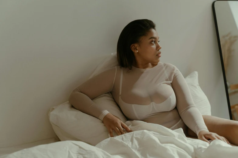 a pregnant woman in a white body suit sitting on a bed