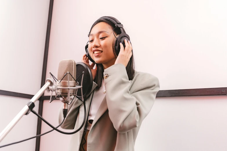 young woman in grey jacket with ear phones standing next to microphone