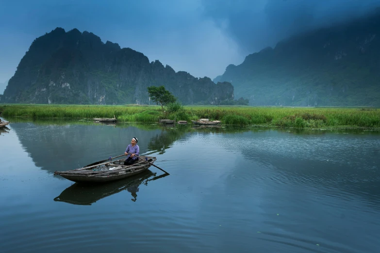 a man sits on the back of a small boat in a calm lake