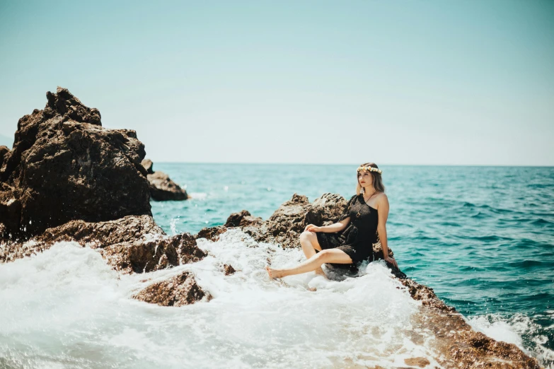 a woman sitting on top of some rocks next to the ocean