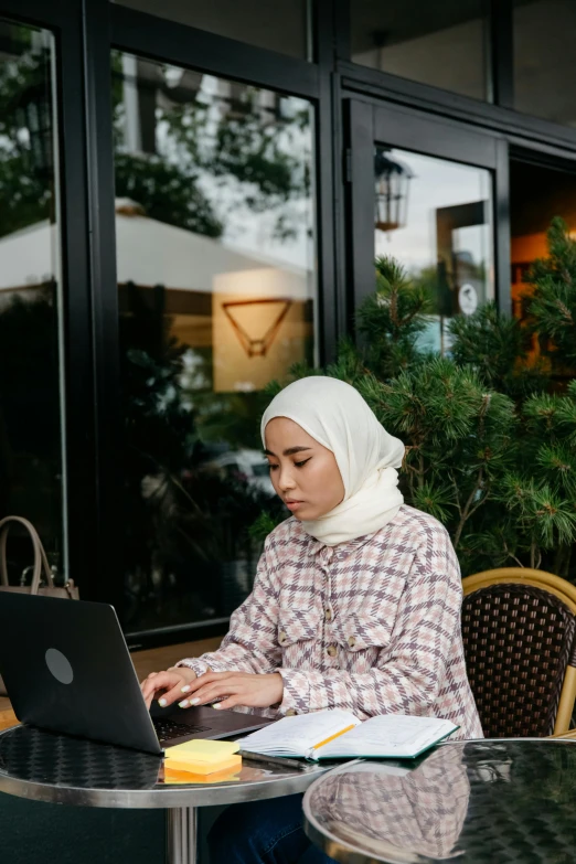 an arab woman is studying outside on her laptop