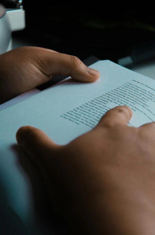 hands hold a book in the sunlight on top of a desk