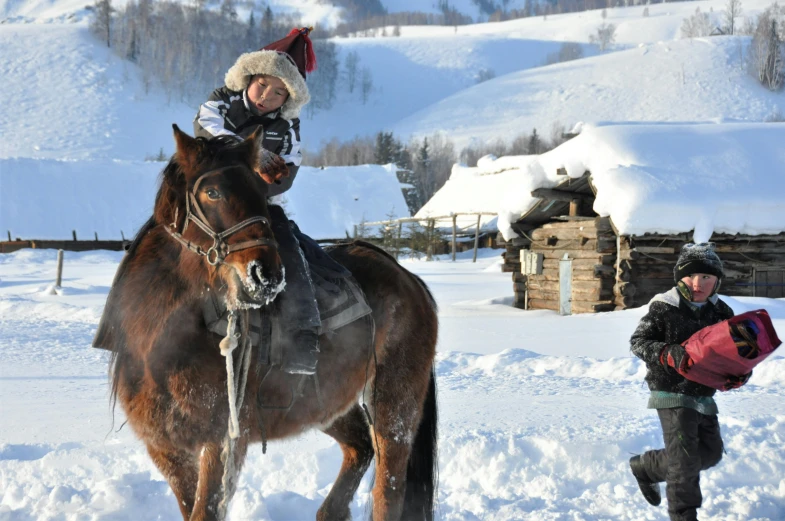 a child rides on top of a horse while a young man is walking behind