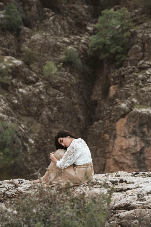 a woman sits on top of the rock and has her hands on her knees