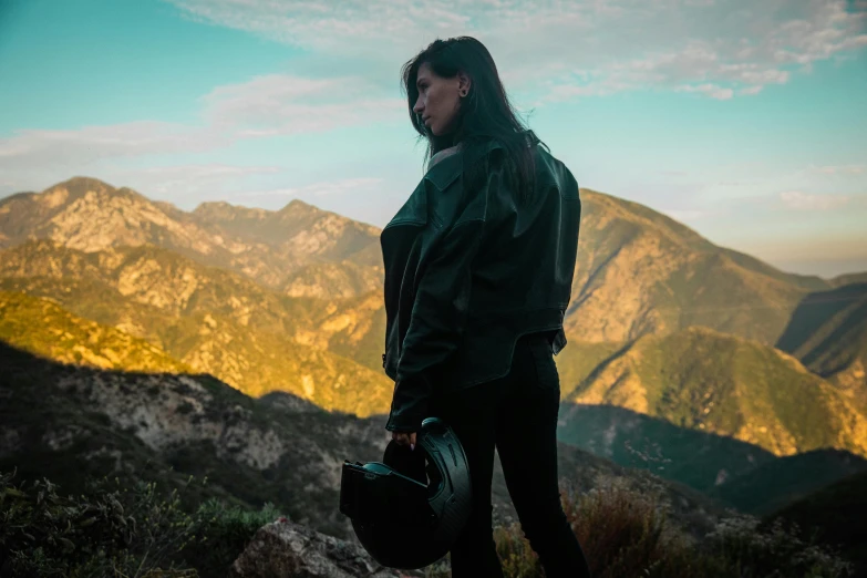 a woman standing with a helmet looking out over a mountain range