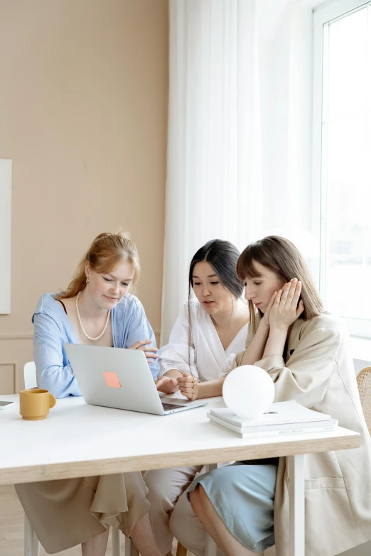 three women are sitting at a table with a laptop