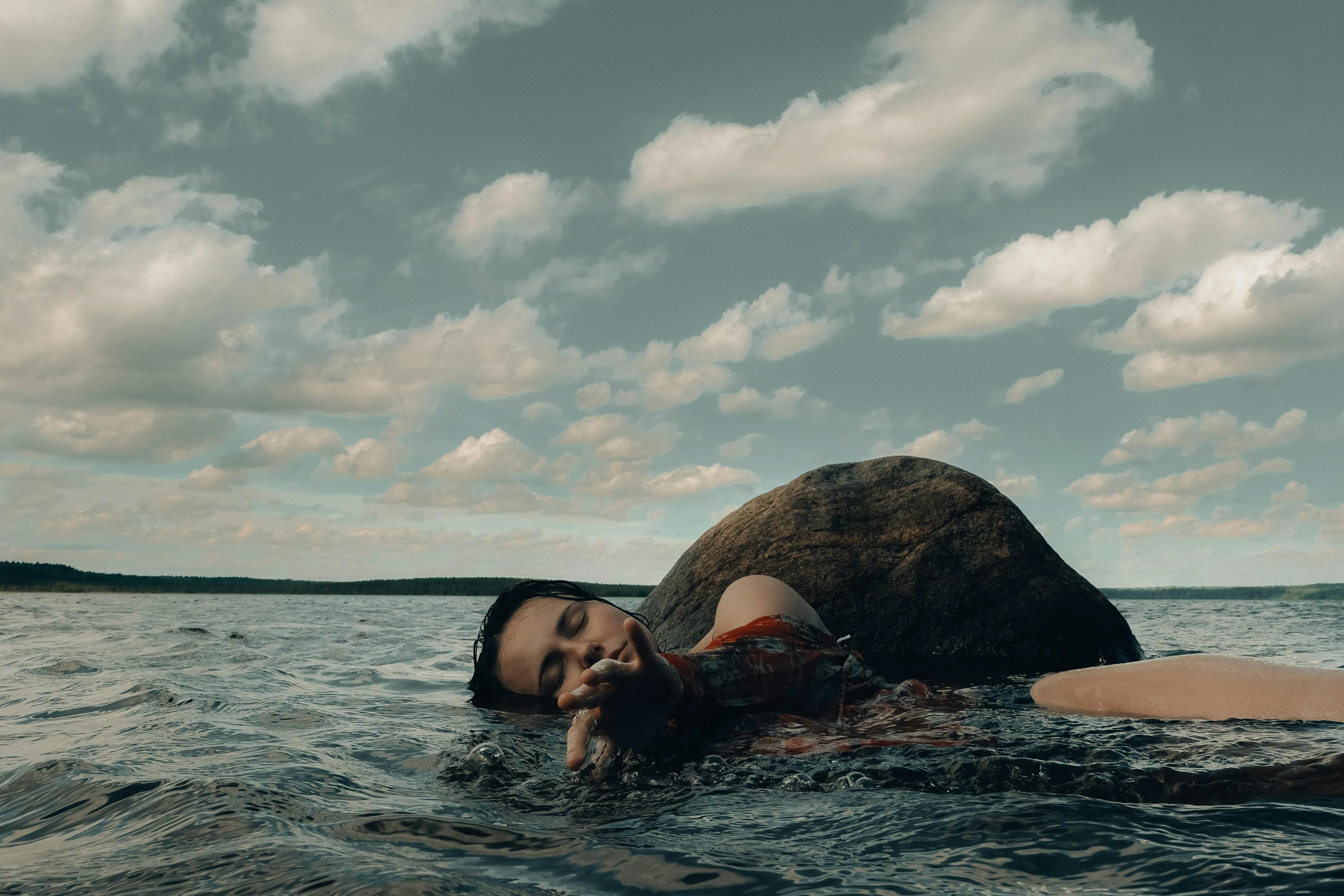 a man in the water with his back to a big rock