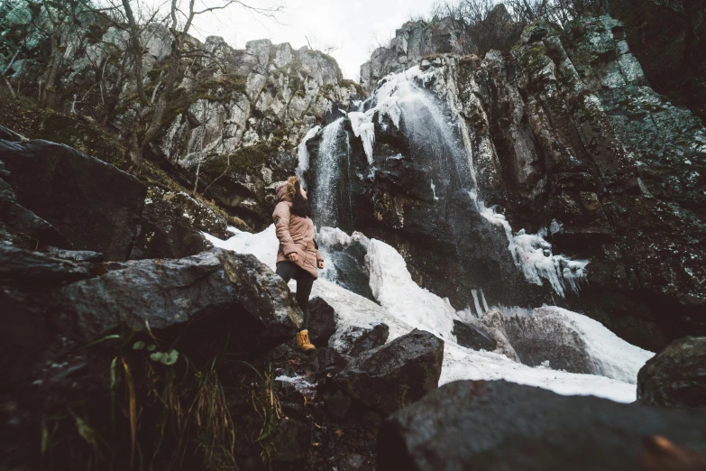 an individual stands near a waterfall with snow