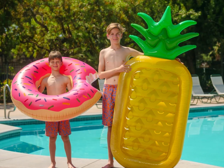 two boys standing near pool with inflatable donuts and water balloons