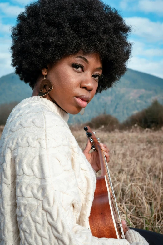 woman with large afro with instrument sitting in tall grass