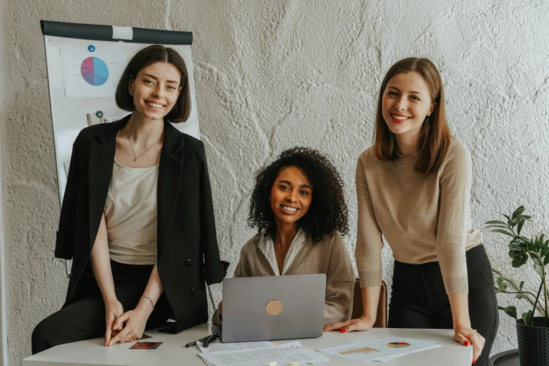 three women pose at a laptop while smiling