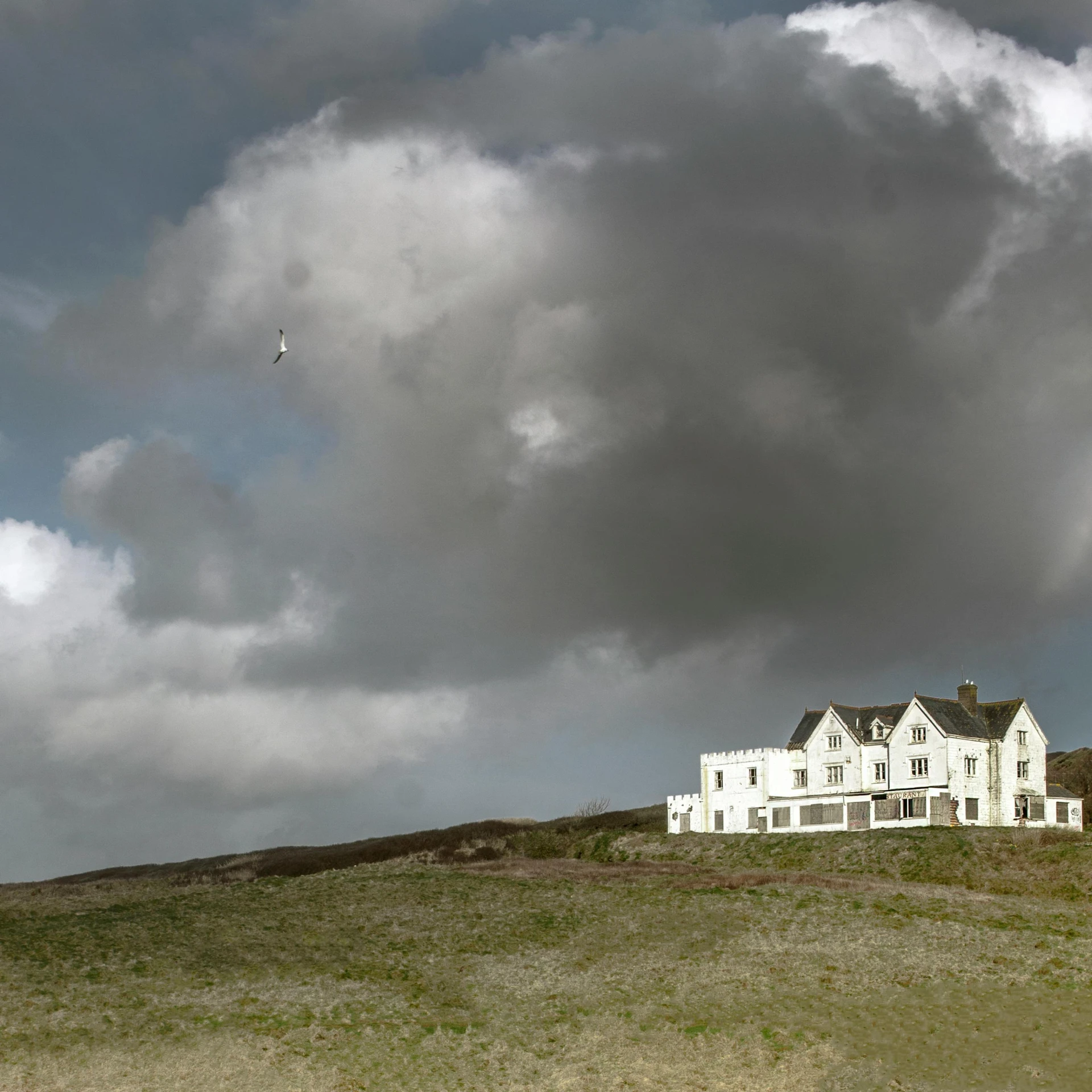 a house is on a grassy hill under a cloudy sky