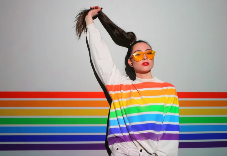 a woman wearing sunglasses and standing against a rainbow striped wall