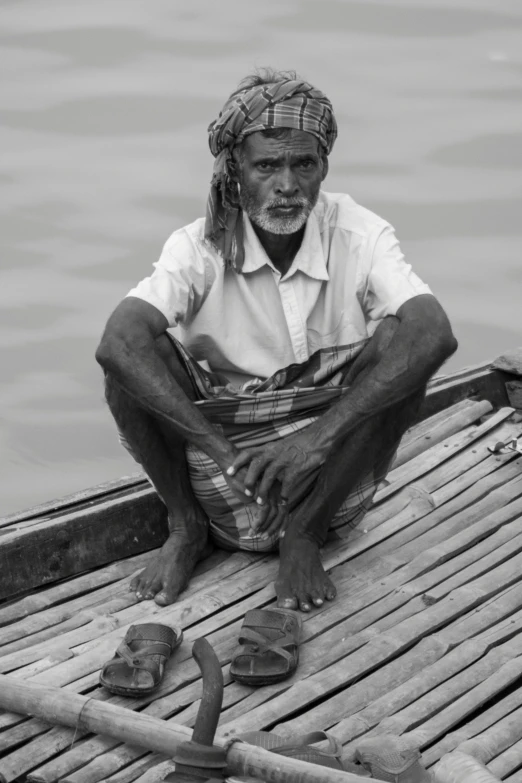 man sitting on bamboo raft with water nearby