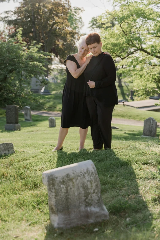 a man and woman stand beside a headstone in a graveyard