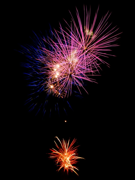 two fireworks are exploding while the dark sky is dark